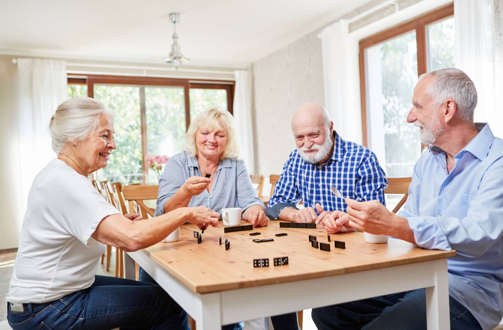 A group of older adults playing dominoes in a sunlit room.
