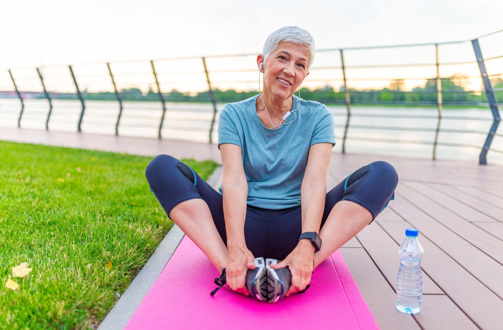 Older adult seated outdoors on a yoga mat practicing flexibility exercises for posture improvement.