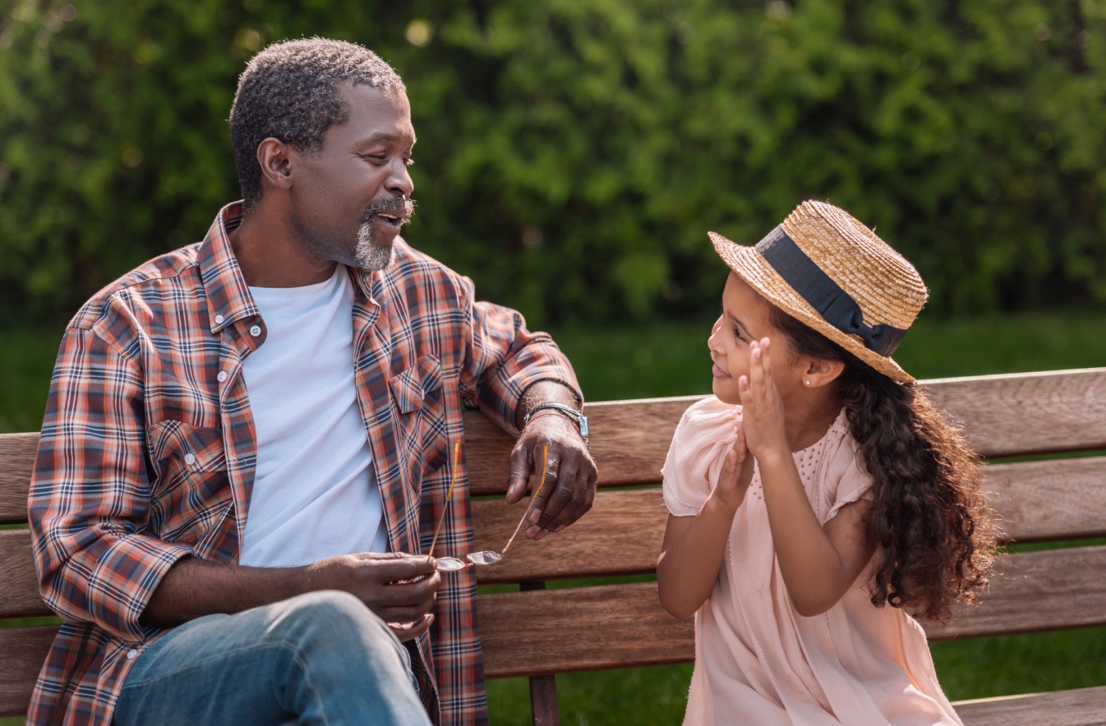 A young child talks to their grandparent while sitting on a bench outdoors.