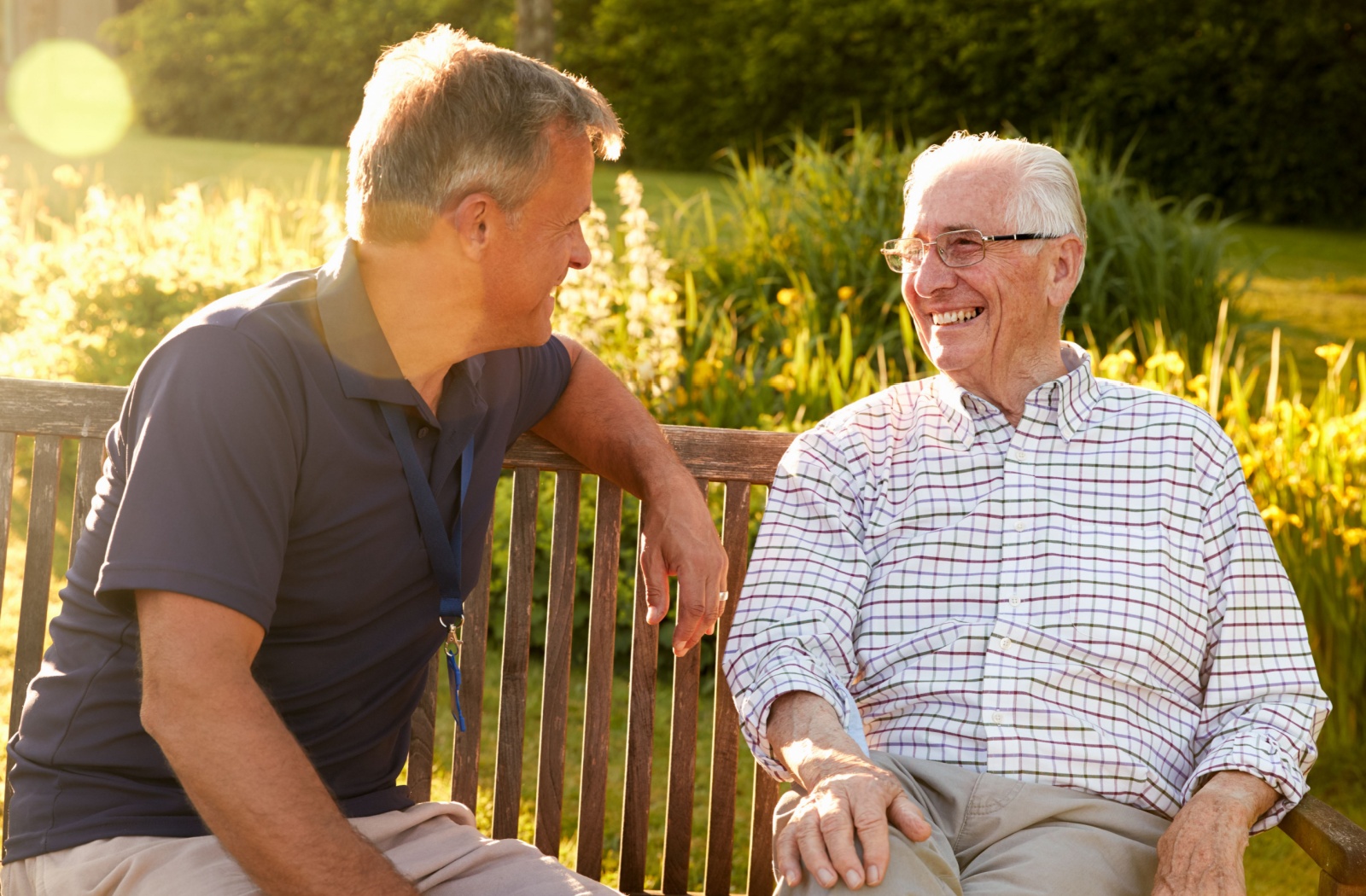 A person talking to a senior in a park on a bench on a sunny day.