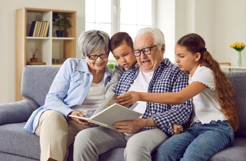 Two children sitting with their grandparents on a couch and going through old photos in an album.