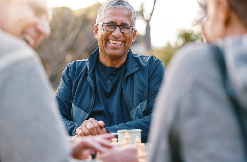 A senior laughs along with two friends while sitting at an outdoor space provided by their senior living community.