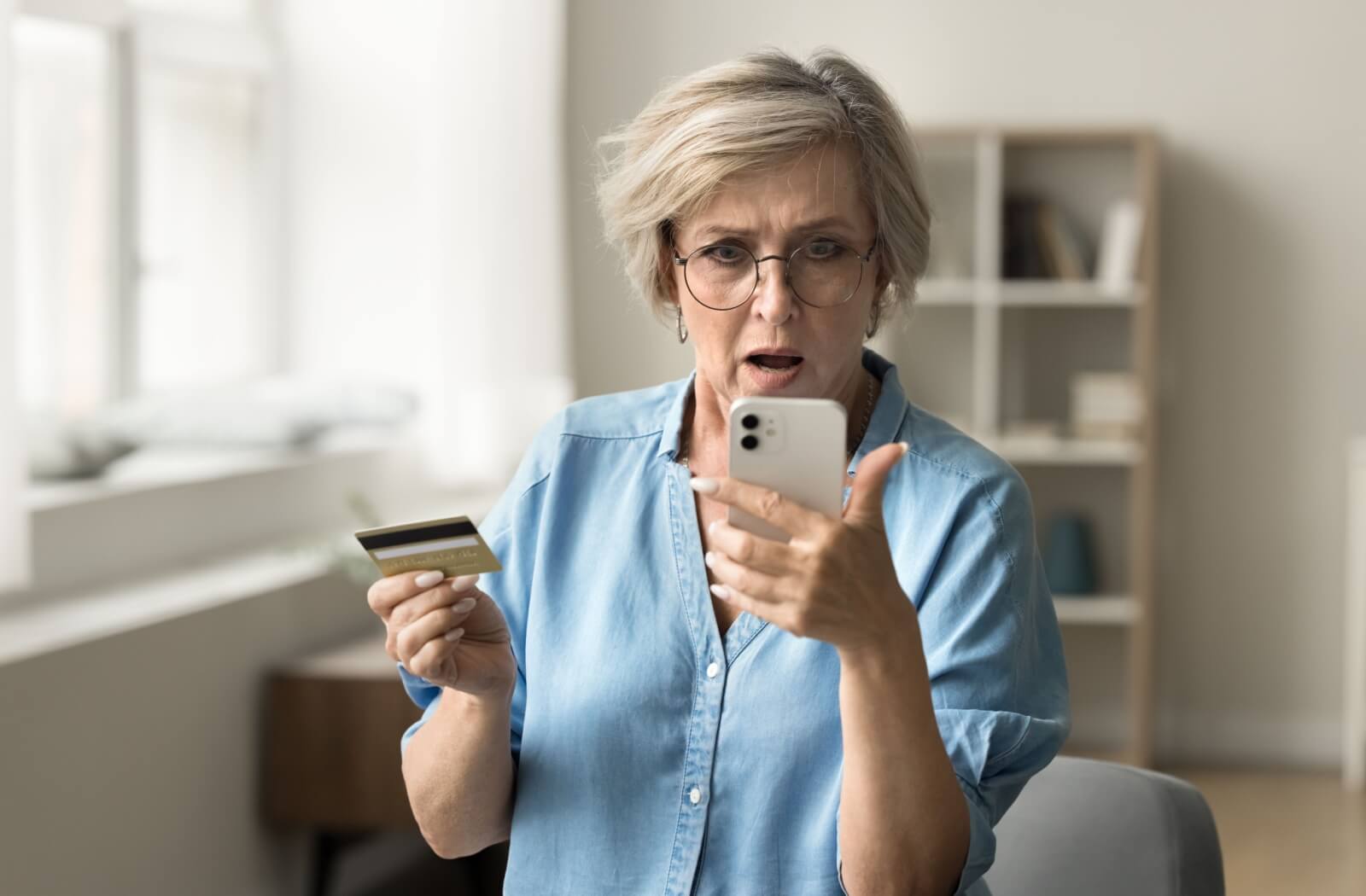 A shocked senior looks at their bank account balance on their phone after being targeted by a financial scam online.