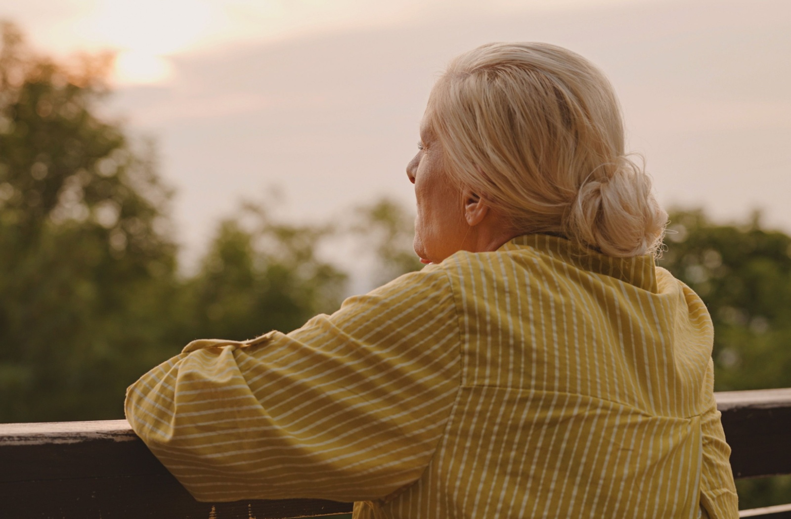 Woman with dementia standing on a porch, looking out at the view.
