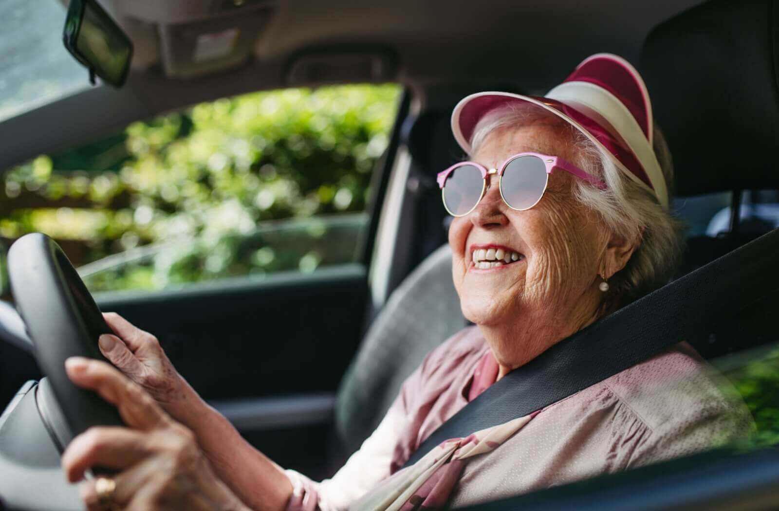 A smiling senior dressed in all pink happily drives themselves to a night of bingo, relishing their independence