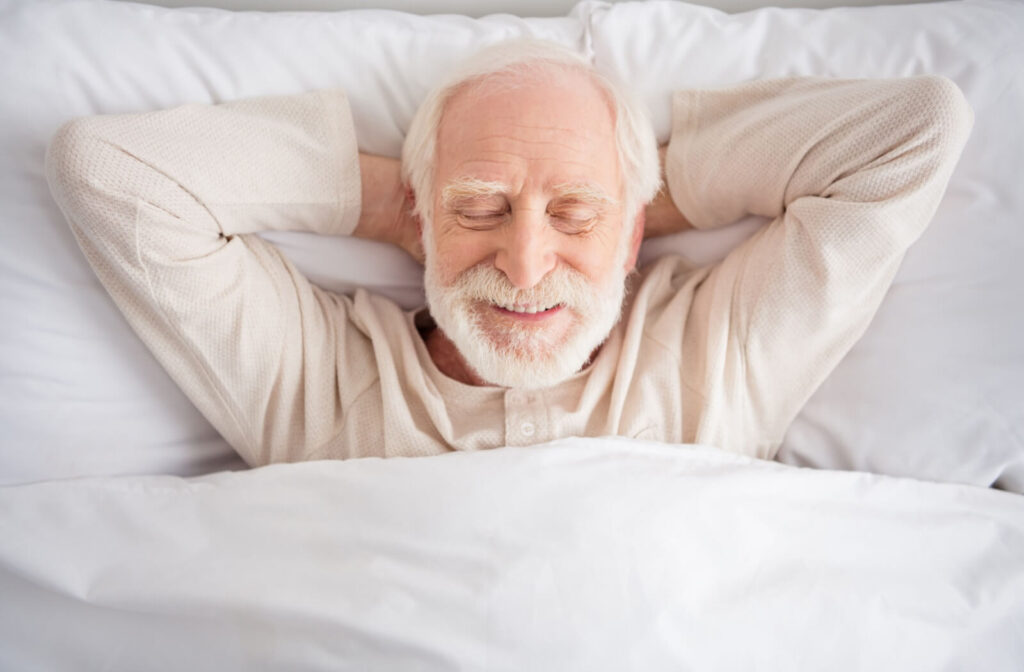 A senior happily settles into a soft, comfortable bed with lush pillows and blankets, ready to have good quality sleep