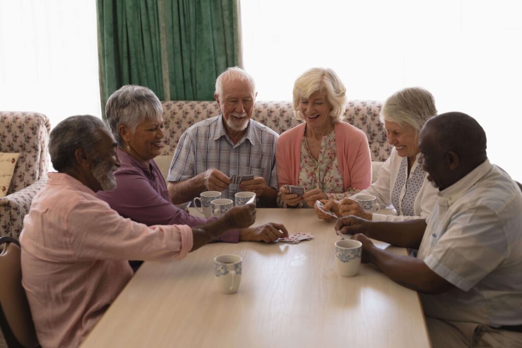 Seniors gathered around a table smiling and playing cards together in a senior living community