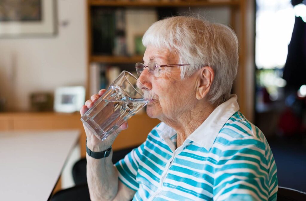 Senior sitting at a table drinking a glass of water at home to maintain daily hydration for health and wellness