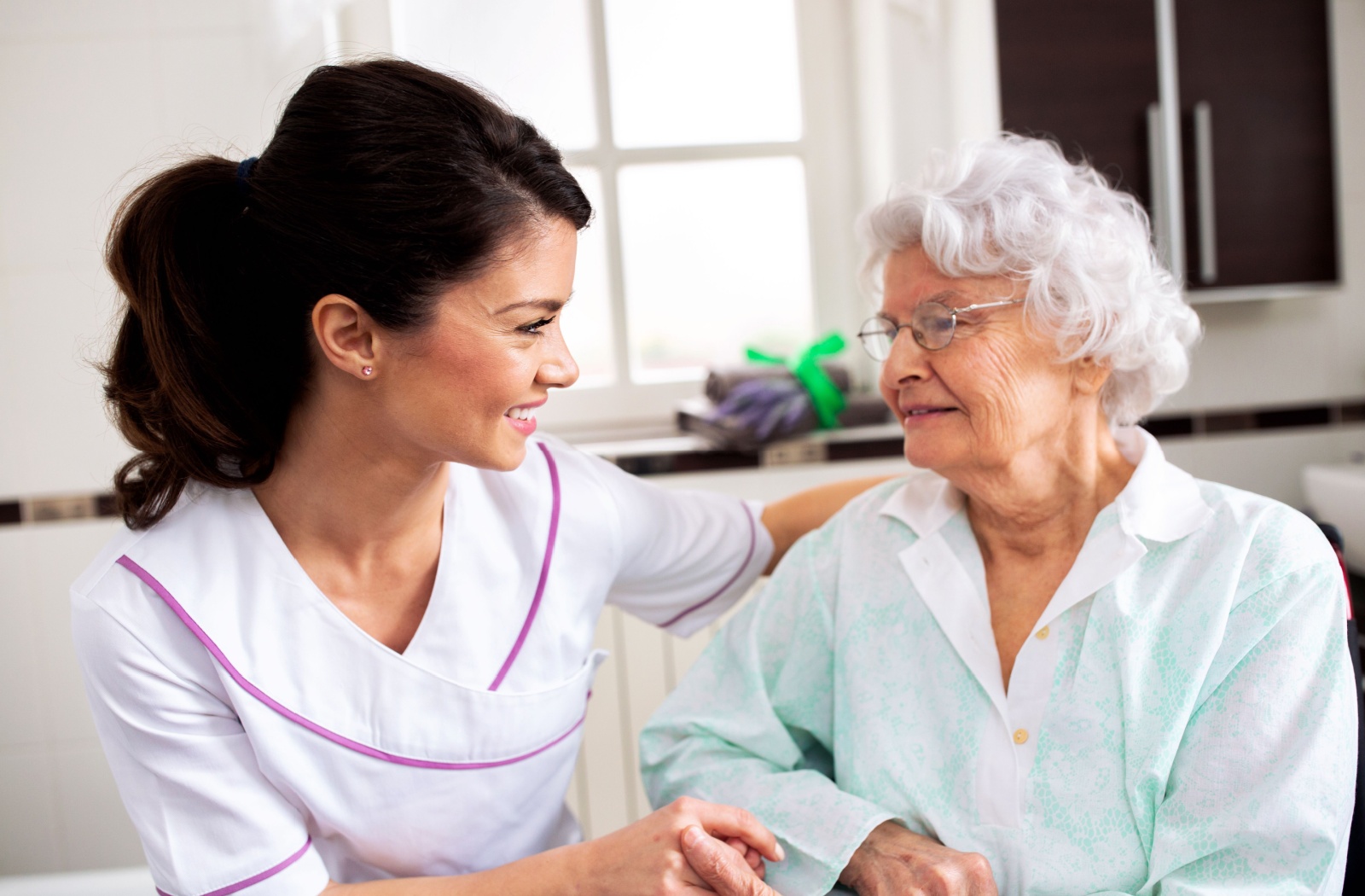 A senior living caregiver sits with a senior, smiling and showing interest while asking about their needs
